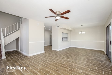an empty living room with a ceiling fan and a staircase