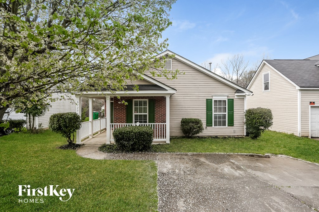 a white house with green shutters and a driveway and a tree