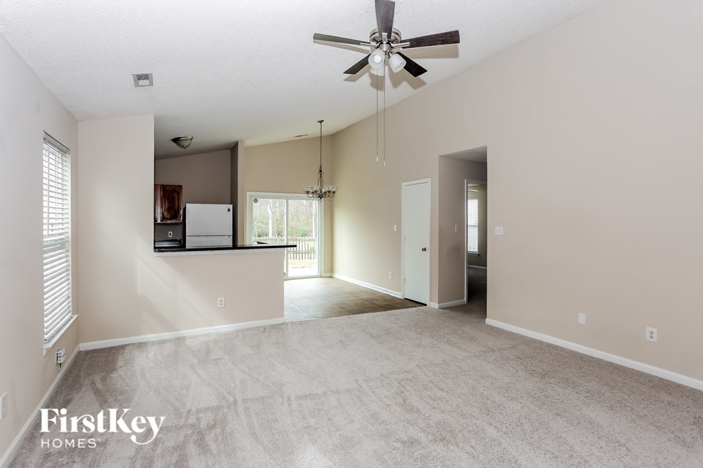 an empty living room with a ceiling fan and a kitchen