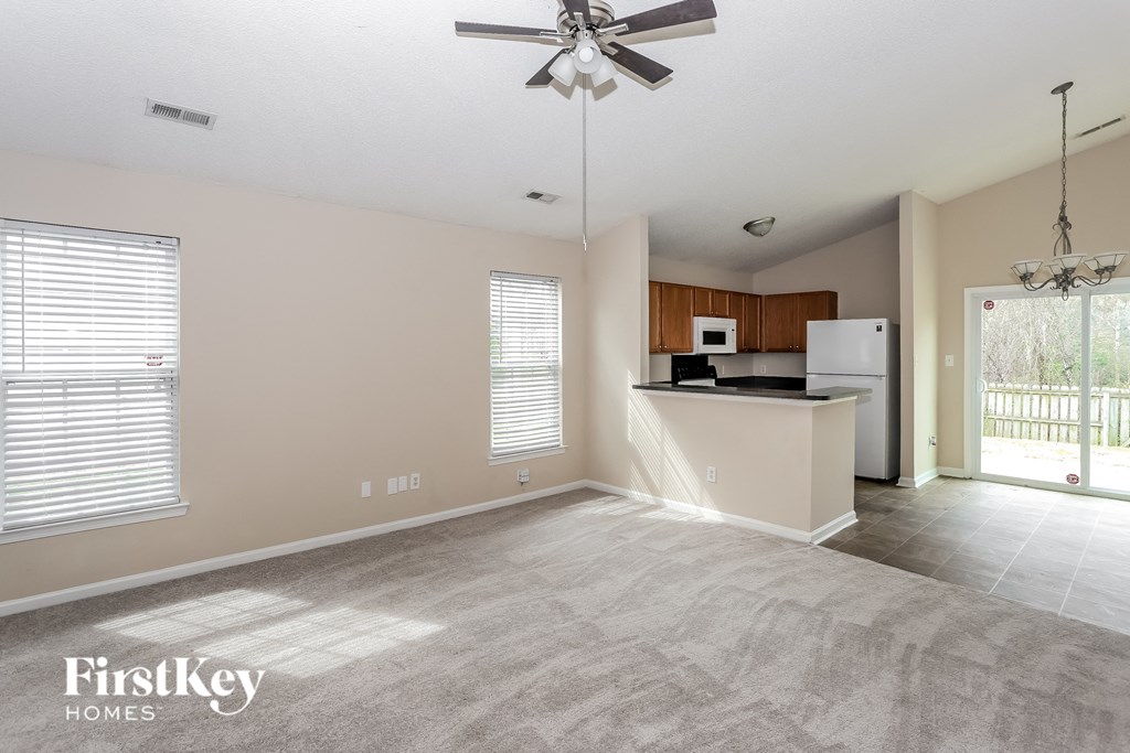 an empty living room with a kitchen and a ceiling fan