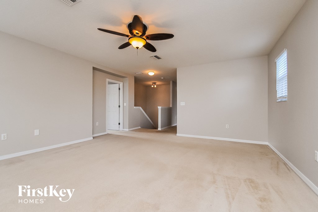 an empty living room with a ceiling fan and a door to a hallway