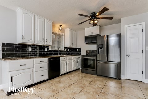 A kitchen with white cabinets and a black tile backsplash.