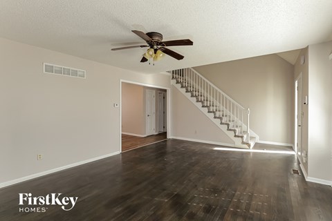 an empty living room with a ceiling fan and a staircase