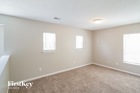 a spacious living room with carpet and two windows