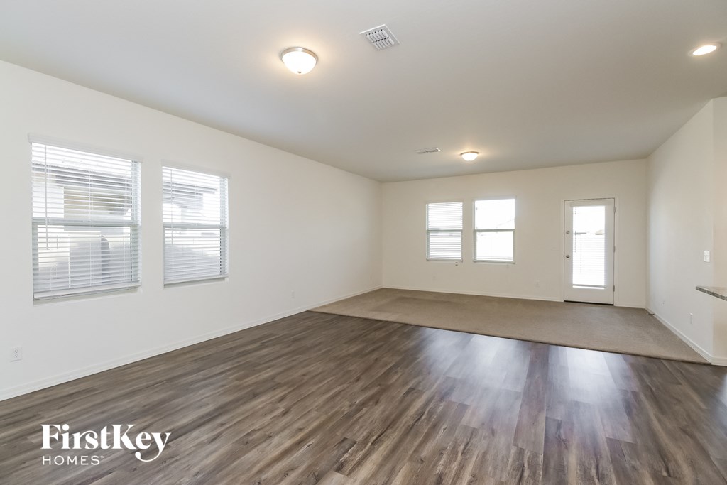 A spacious room with wooden flooring and three windows.