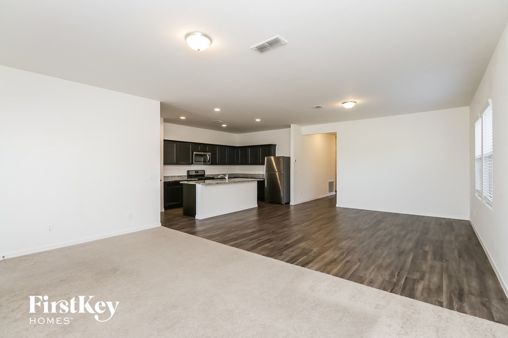 A spacious room with wooden floors and a kitchen area in the background.