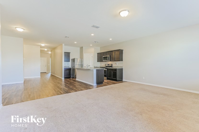 an empty living room with a kitchen in the background