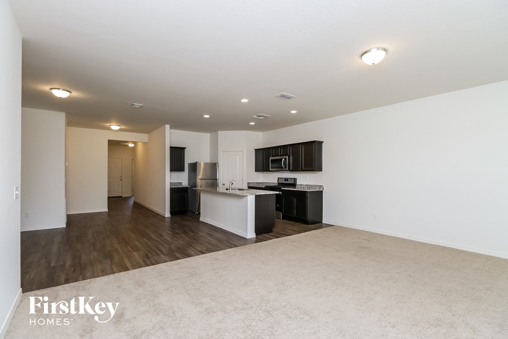 the living room and kitchen of an apartment with white walls and wood flooring
