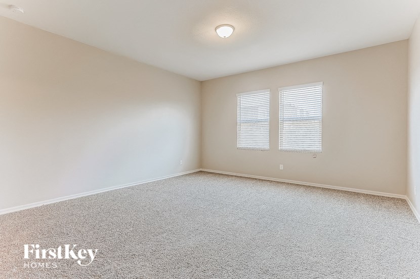 a spacious living room with white carpet and two windows