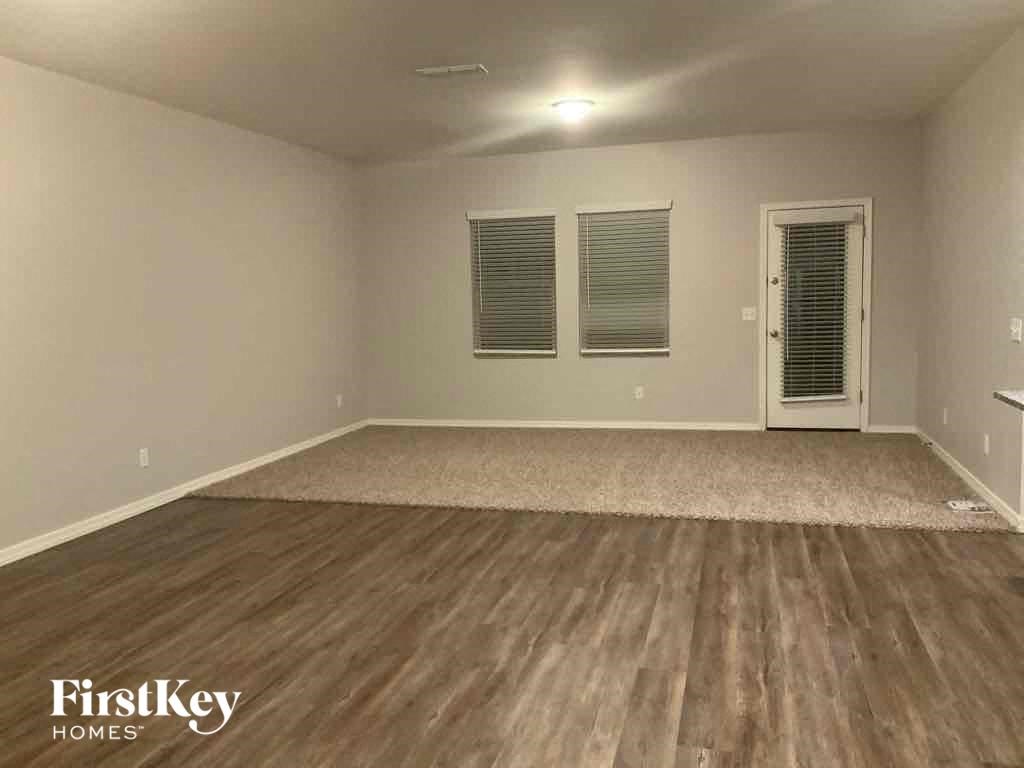 an empty living room with hardwood flooring and a door to the kitchen