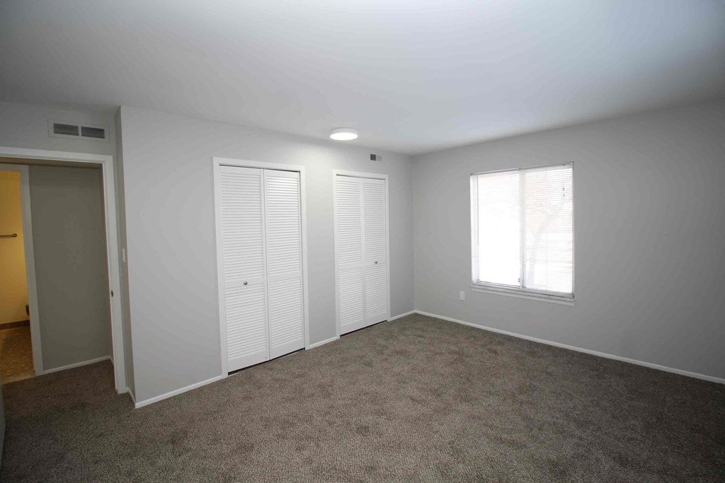 A room with a carpeted floor, a window, and a door.