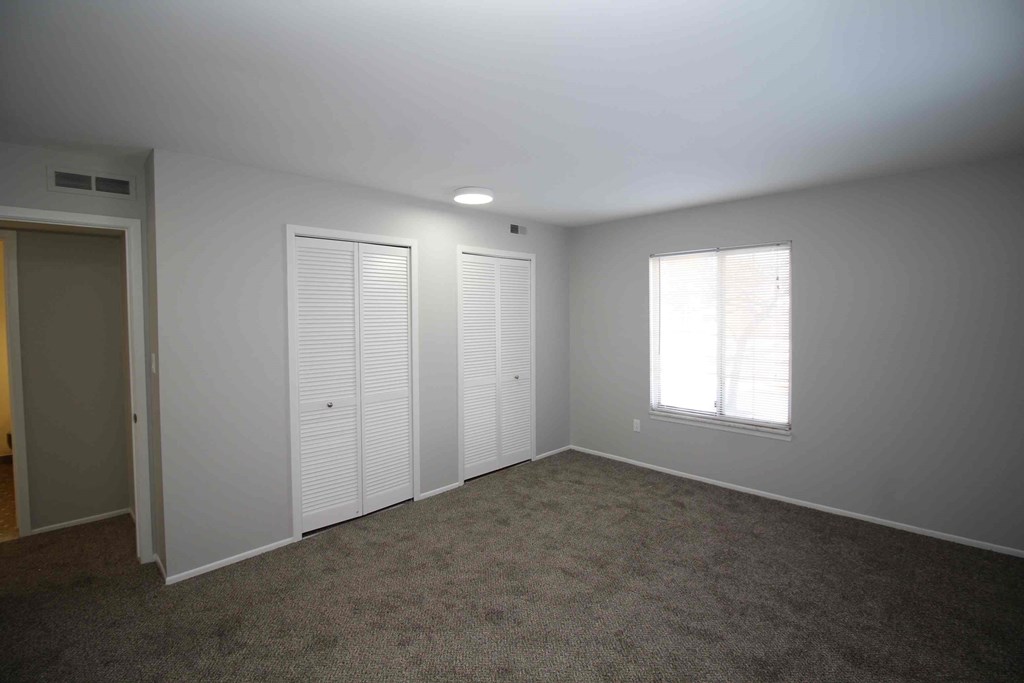 A room with a carpeted floor, two closets, and a window with blinds.
