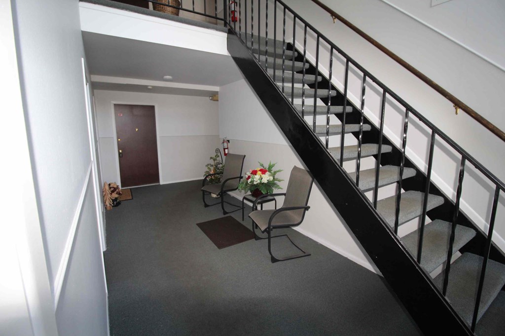 A black metal staircase with a white wall and a brown door.