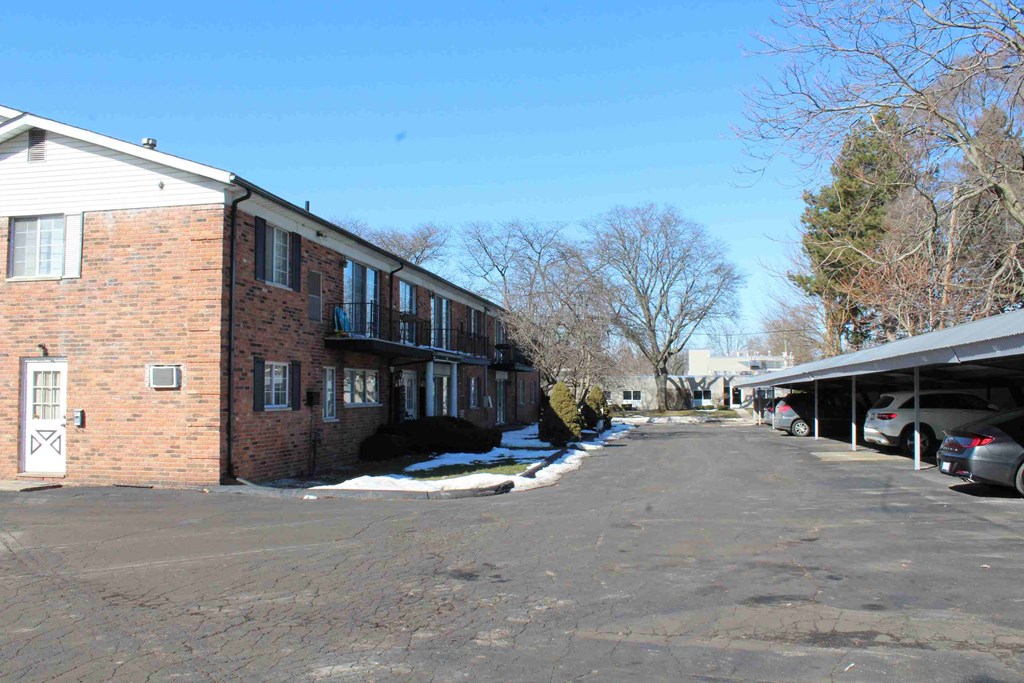 A parking lot in front of a brick building with a car parked in the lot.