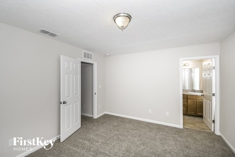 a bedroom with white walls and carpet and a door to a bathroom