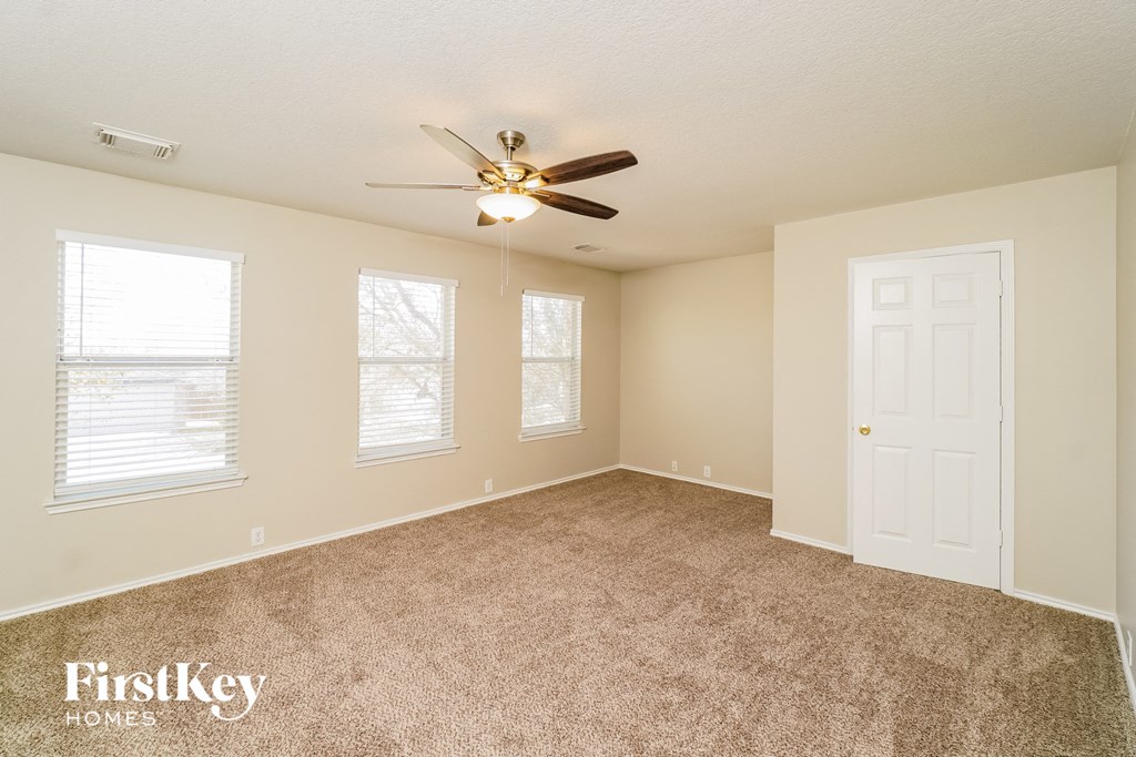 an empty living room with a ceiling fan and three windows