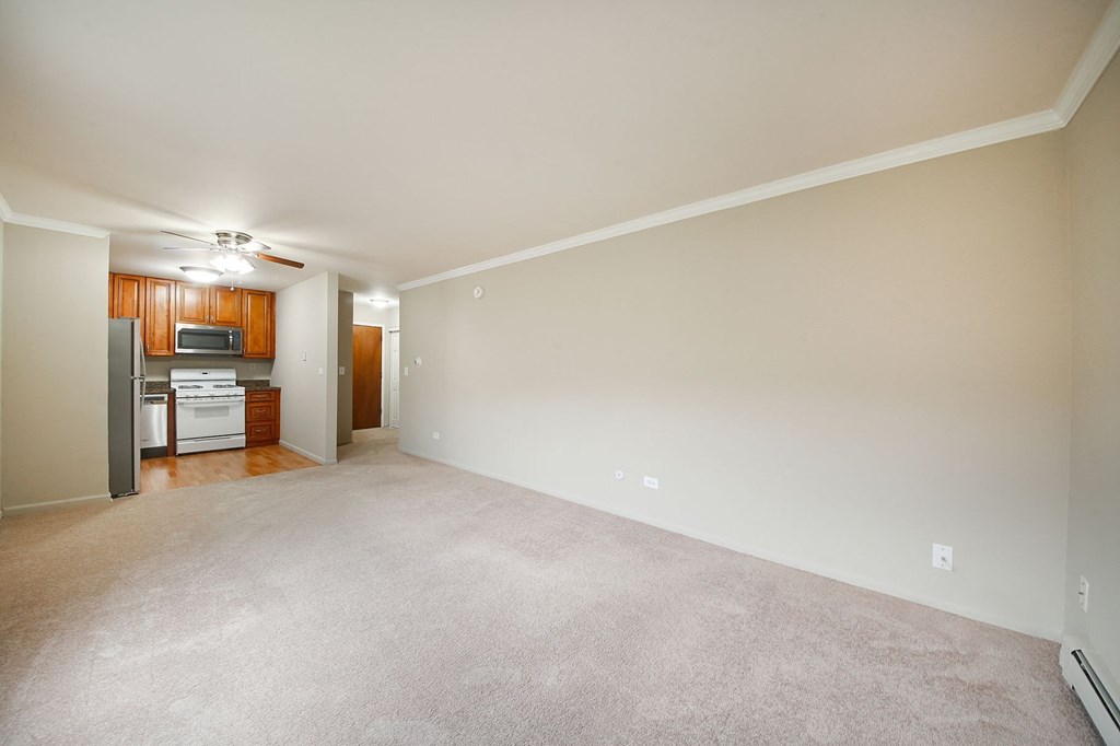 an empty living room with a kitchen in the background