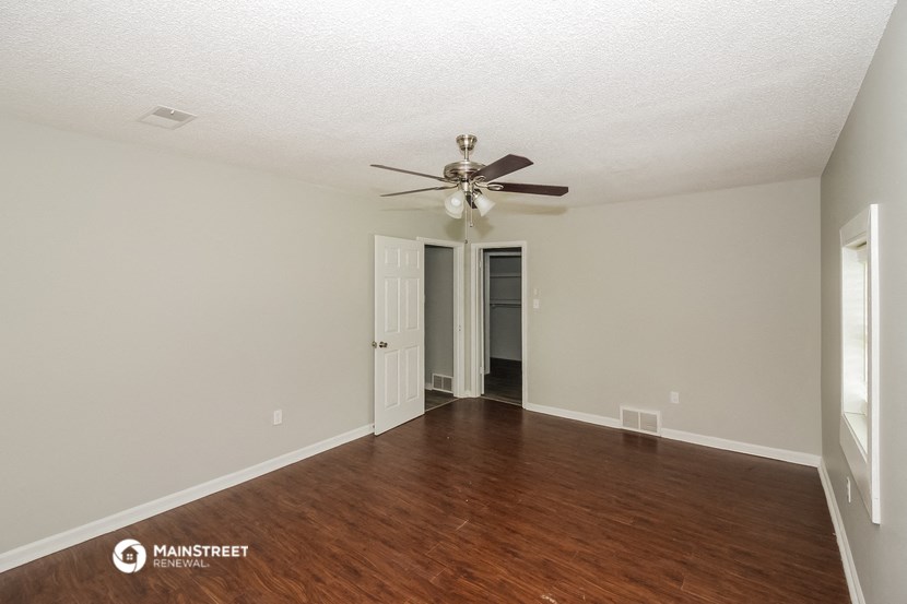 the spacious living room with wood flooring and a ceiling fan