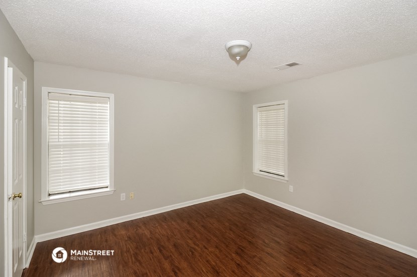 the interior of an empty room with wood flooring and two windows