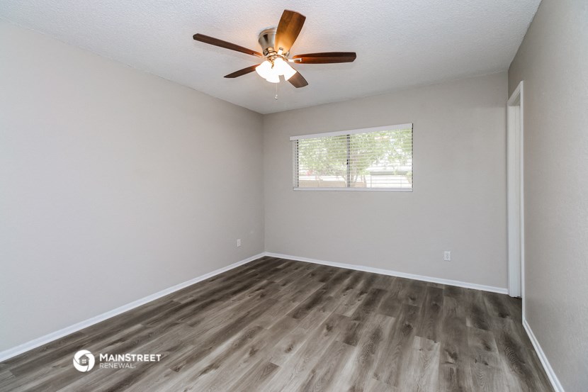 the spacious living room with wood flooring and a ceiling fan