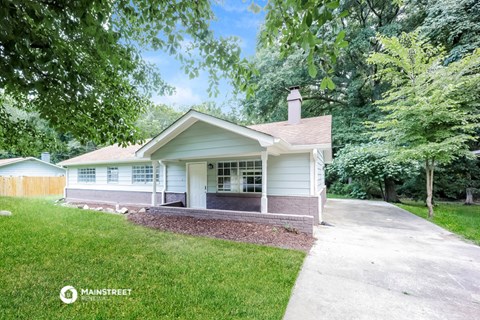 a small white house with a driveway and trees