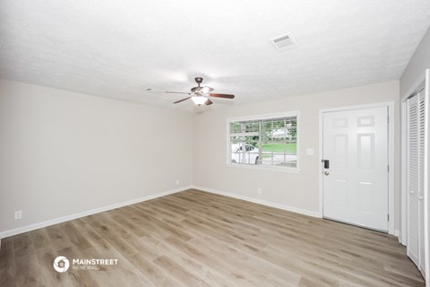 the spacious living room with white walls and a ceiling fan