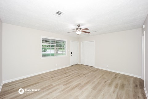 the spacious living room with hardwood floors and a ceiling fan