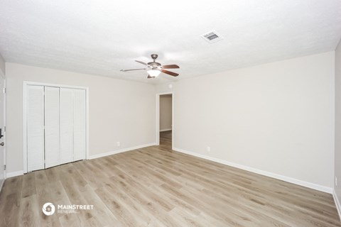 the spacious living room with wood flooring and a ceiling fan