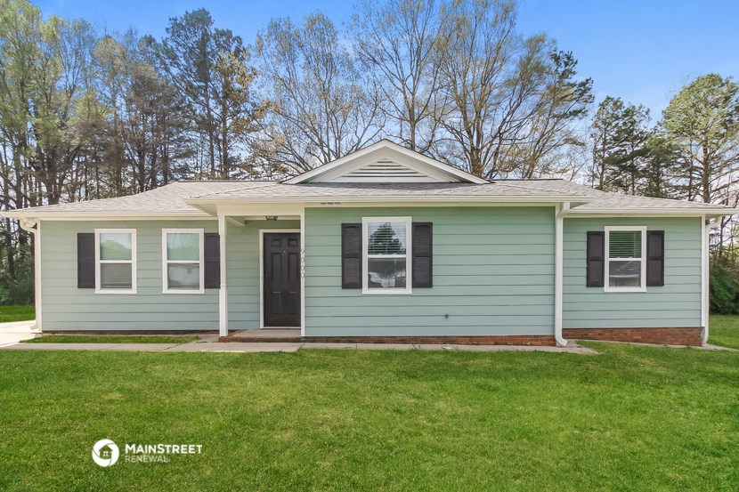 a green house with a lawn and trees behind it