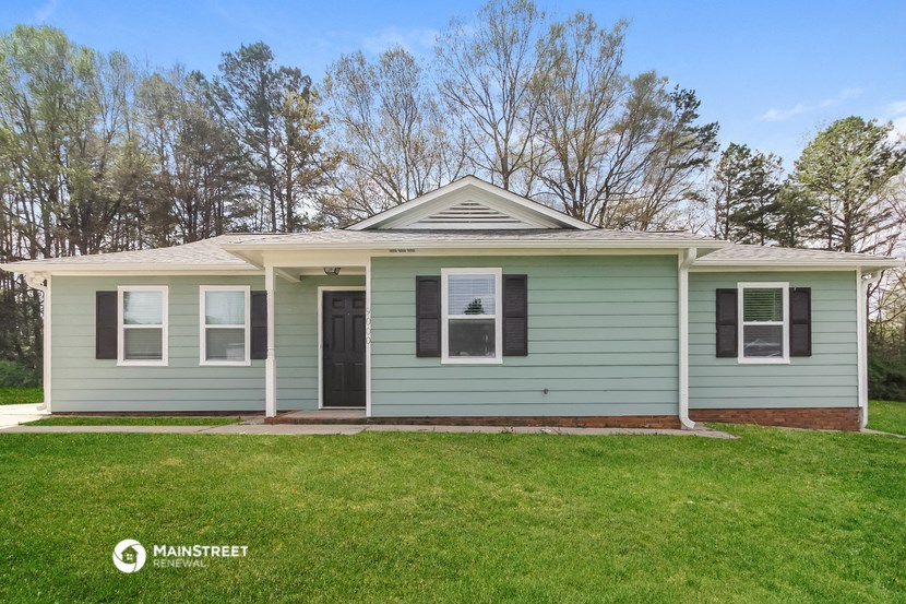 a green house with a lawn and trees in the background