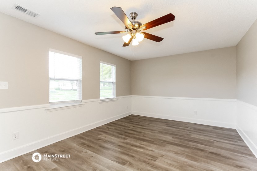 an empty living room with a ceiling fan and two windows
