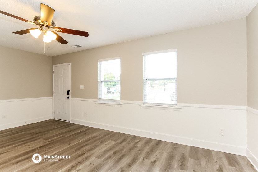 an empty living room with a ceiling fan and two windows