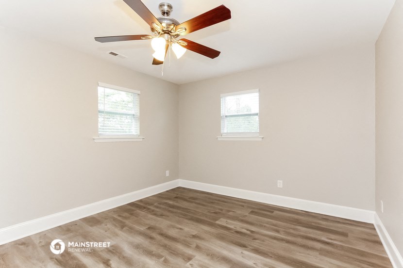 an empty room with a ceiling fan and two windows