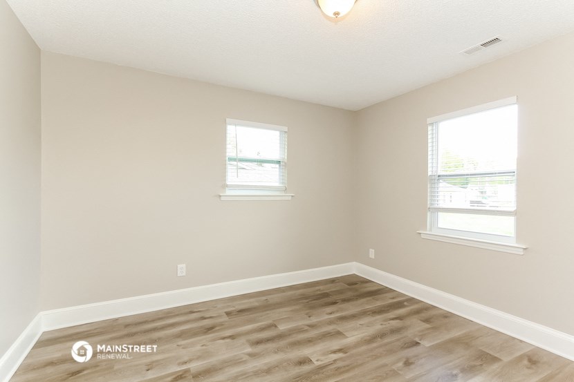 a living room with a wooden floor and two windows