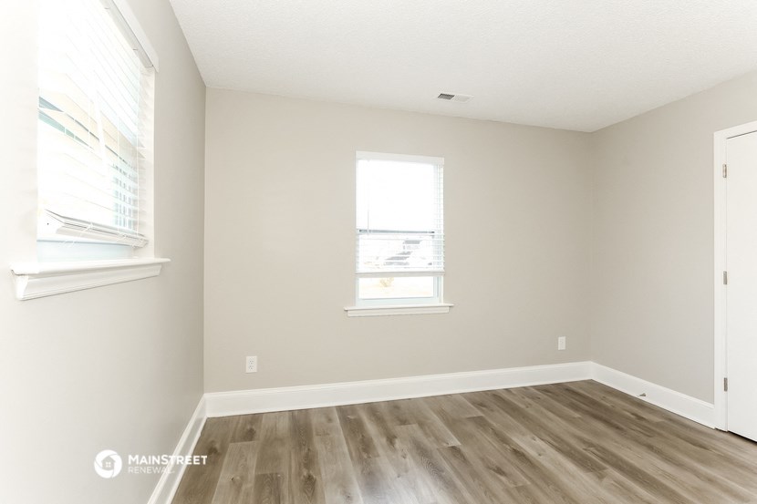an empty room with wood floors and two windows