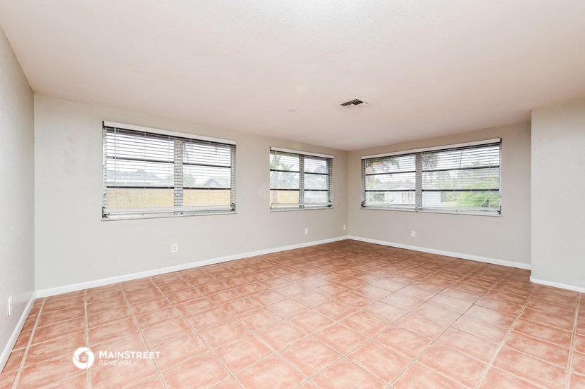 an empty living room with three windows and a tiled floor