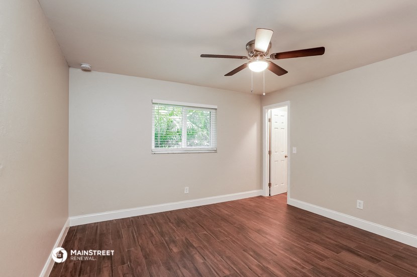 the spacious living room with hardwood flooring and a ceiling fan