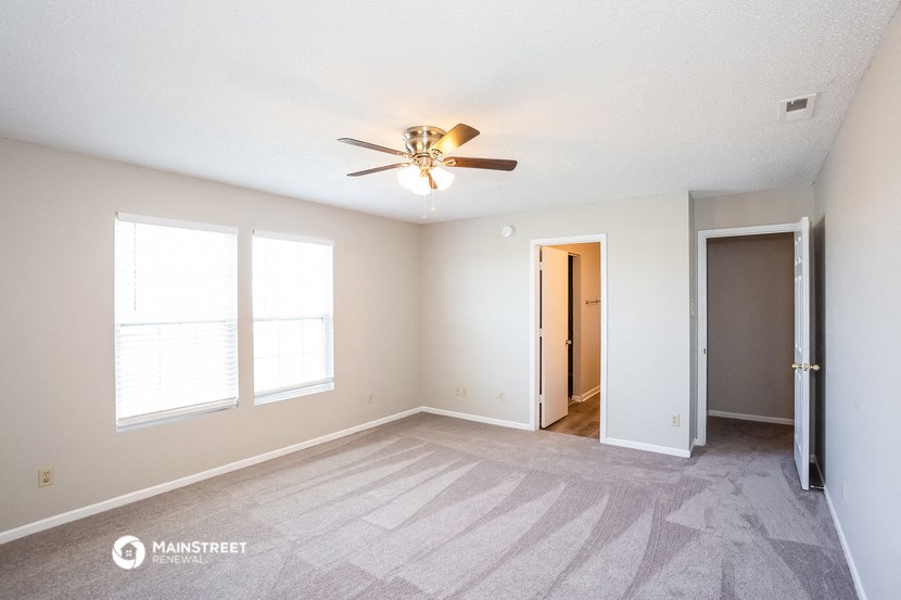 an empty living room with a ceiling fan and two windows