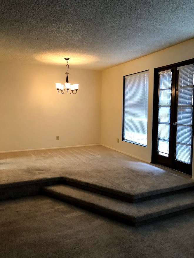 an empty living room with a chandelier and a window