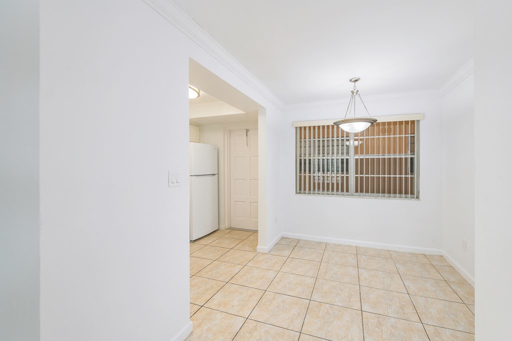 an empty living room and kitchen with a window and a refrigerator