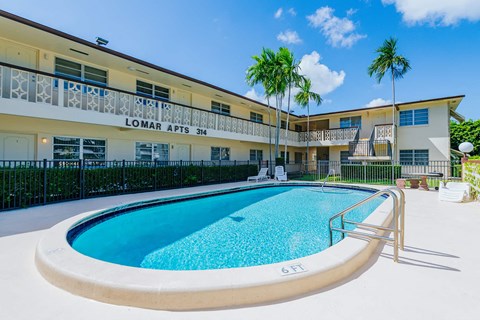 a swimming pool in front of a building with palm trees