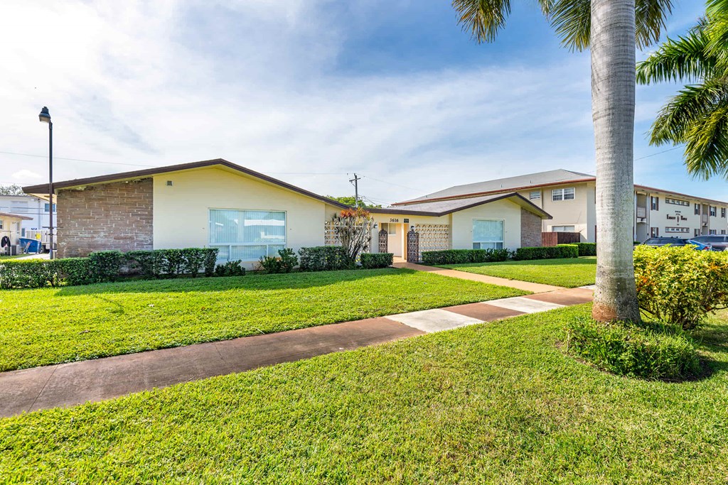 a sidewalk in front of a house with grass and palm trees
