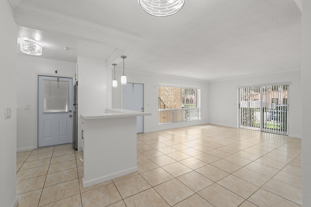 the living room and kitchen of a house with tiled flooring and a counter