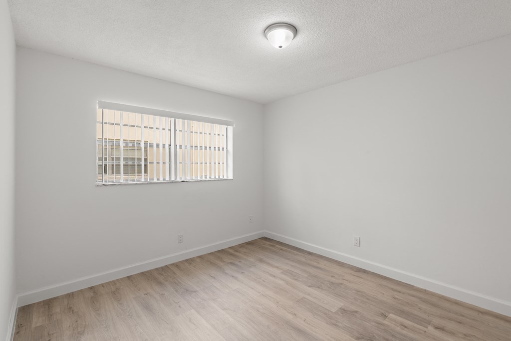 a bedroom with white walls and wood flooring and a window