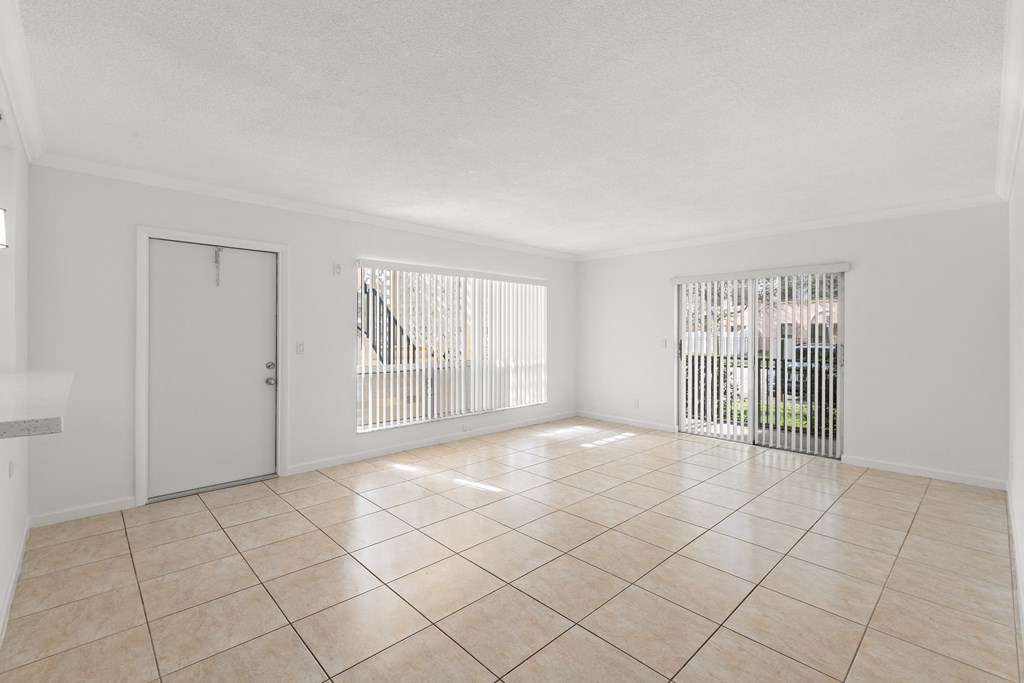 an empty living room with tiled floors and a door to a balcony