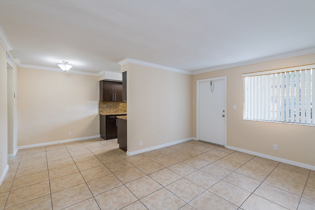 an empty living room with tile flooring and a door to a kitchen