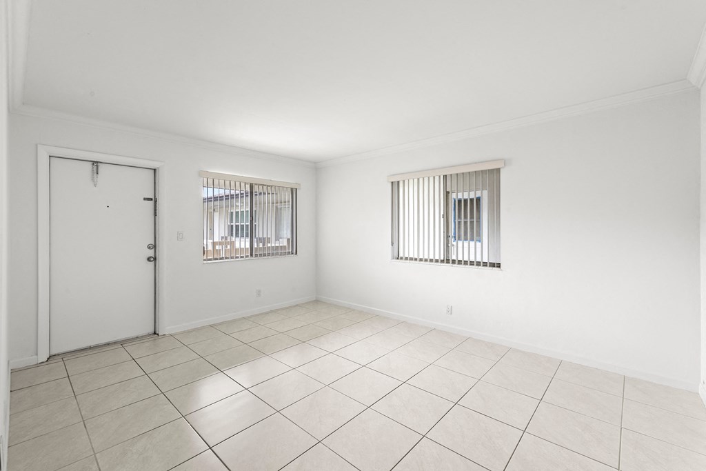 the living room of a house with white walls and tiled floor and a door