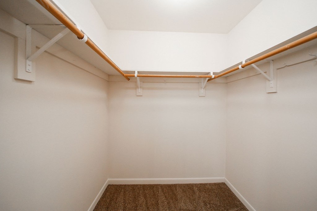 an empty closet with white walls and a brown rug and white pipes on the ceiling