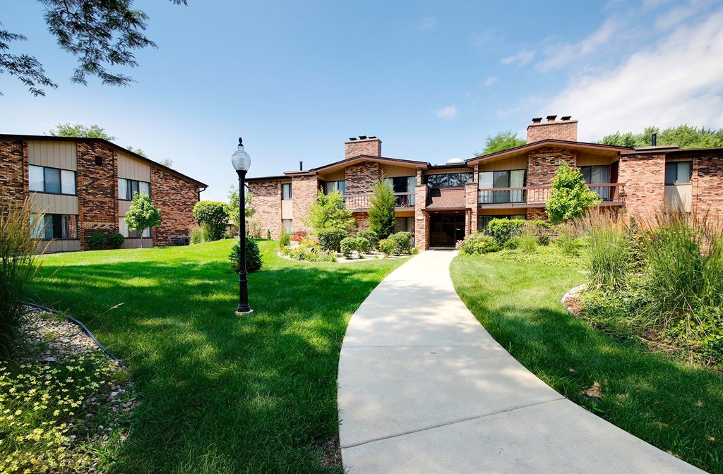 a sidewalk in front of a building with green grass and trees