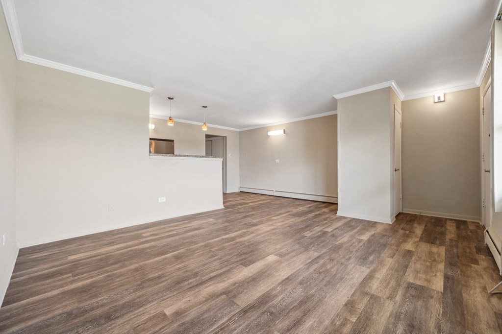 an empty living room with wood flooring and a kitchen